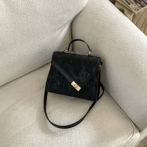 Detail of black textured handbag with a gold rectangular swivel lock on a soft sofa