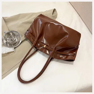 Vue de dessus du sac cabas en cuir brillant marron foncé avec boucle dorée sur tissu blanc