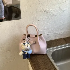 Detail of light pink bucket bag with decorative leather belt and plush bear charm