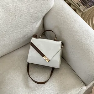 Detail of minimalist two-tone leather handbag with golden buckle on a textured sofa
