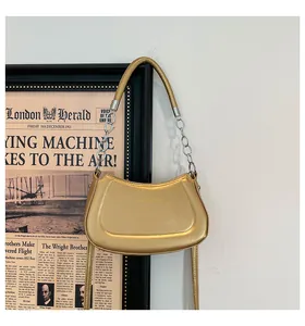 Detail einer goldenen Metallic-Halbmondtasche mit eleganter Kette und modischem Schriftzug