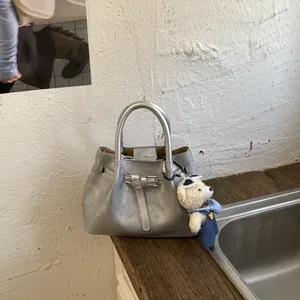 Detail of silver bucket bag with strap buckle and cute bear charm on a wooden surface