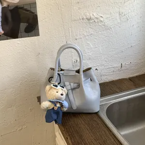 Detail shot of light blue bucket bag with belt buckle and cute teddy bear charm accessory