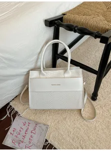 Dettaglio borsa bianca con trama a coccodrillo e scritta Fashion & Bags sul letto