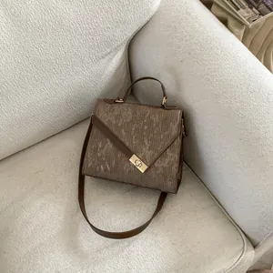 Detailed close-up of brown textured leather square bag with gold geometric twist lock