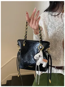 Detail of black quilted bucket bag with gold chain handle and a white horse charm