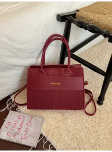 Dettaglio borsa tote bordeaux con stampa serpente e logo dorato su tappeto
