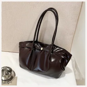 Détail du sac seau en cuir brillant marron foncé avec boucle dorée et design plissé