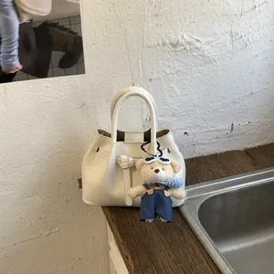 Close-up of cream bucket bag featuring belt buckle detail and a cute plush bear charm