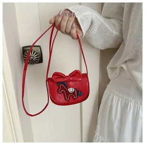 Detail van rode crossbodytas met strik, paardenborduursel en gewatteerde textuur