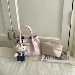 Light pink bucket bag with leather strap detail and cute bear charm on white surface