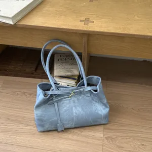 Detail of light blue tote bag with matte texture and metallic buckle on wooden bench