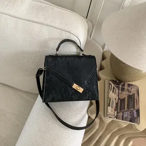 Detail of a black textured crossbody bag with gold clasp on a minimalist sofa