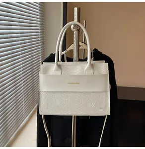 Dettaglio della borsa bianca a motivo coccodrillo con scritte dorate e manico curato