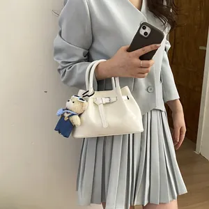 Creamy white leather bucket handbag with teddy bear charm and belt strap detail