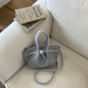 Close-up of a light blue woven bucket bag with leather strap buckle on a white sofa