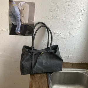 Detail of matte dark grey tote bag with slim strap and small metal buckle on wood table