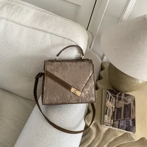 Detail of tan metallic fabric texture and gold twist lock on women's handbag