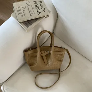 Close-up of khaki woven bucket bag with metallic buckle on white textile background