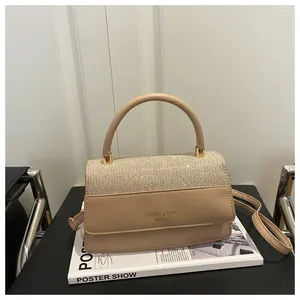 Detail of glitter flap on light brown handbag with metal hardware and top handle