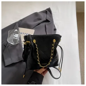 Detail of black quilted bucket bag with gold chain and drawstring closure on a gray blazer