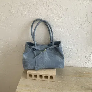 Detailed view of Morandi blue suede tote bag with matte texture on stone pedestal