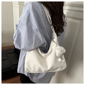 Close-up of a white hobo underarm bag with a cute plush bear pendant and silver zipper
