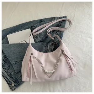 Detalle de bolso de hombro rosa claro con cadena de perlas y cremalleras decorativas