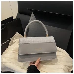 Detail of light grey square bag featuring a glittery flap and elegant gold handle