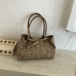 Detail view of a retro tan tote bag featuring smooth texture and elegant strap buckle on stone