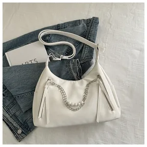 Detalle de un bolso de media luna blanco con cadenas plateadas, perlas y cremalleras