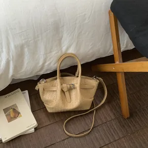 Top view of beige woven bucket bag with knot detail on white bedding and wood floor