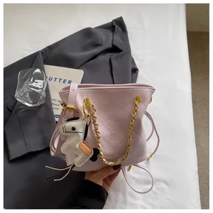Detail of pink quilted bucket bag with gold chain and horse charm on grey blazer