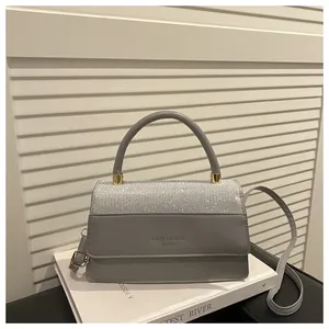 Detail of grey paneled handbag featuring round handle and gold hardware on white pedestal