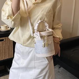 Borsa a secchiello beige con ricamo in pizzo e foulard decorativo mostrata su un modello