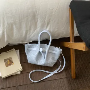 Detail of light blue woven bucket bag with metallic buckle and slim shoulder strap