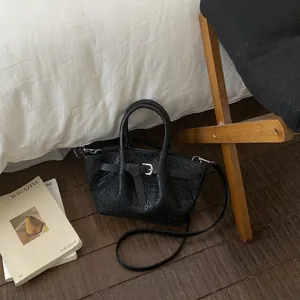 Detail of black woven bucket bag with silver buckle on wooden floor background