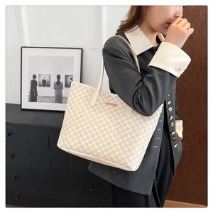Detail of beige tote bag with letter M pattern and gold logo plate on a model