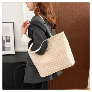 Detail of apricot tote bag featuring repetitive letter M pattern and gold logo plaque