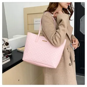 Close-up of pink tote bag with M-pattern print and gold logo tag in a cafe setting
