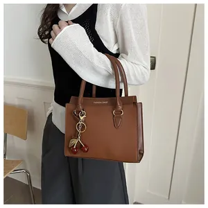 Détail d'un sac à main carré en cuir caramel avec texture litchi et bijou de sac cerise