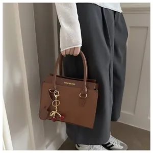 Détail d'un sac carré marron texture cuir avec un pendentif cerise en métal rouge