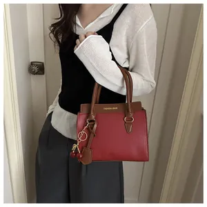Détail du sac bandoulière bicolore rouge et marron avec texture lychee et pendentif cerise