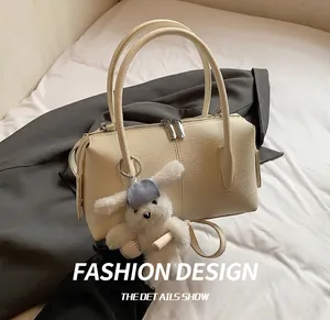 Detail showing off-white litchi grain leather Boston bag with double zippers and plush charm