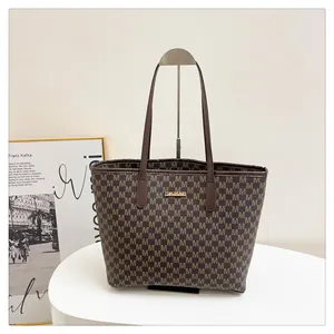 Close-up of brown tote bag with all-over letter pattern and gold logo plaque detail