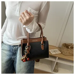 Détail du sac en cuir grainé noir avec poignée marron et breloque cerise rouge décorative