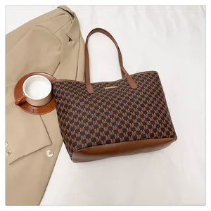 Detail view of large brown monogram tote bag on white fabric background with casual props