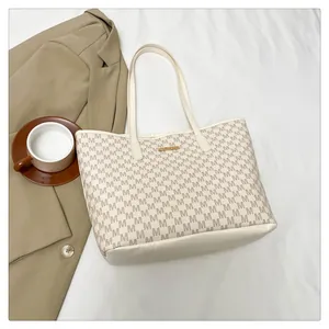 Macro view of beige tote bag featuring letter print and gold metal logo plaque detail