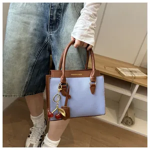 Détail du sac à main bleu clair en cuir grainé avec rabat marron et breloque cerise