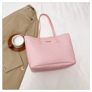 Close-up of pink tote bag with letter prints and gold hardware in an office setting